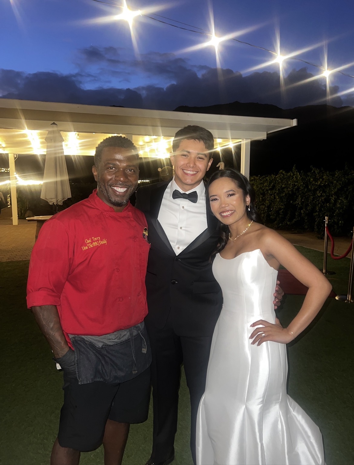 Chef Terry in red BBQ Daddy chef coat with bride and groom at a San Diego County outdoor wedding