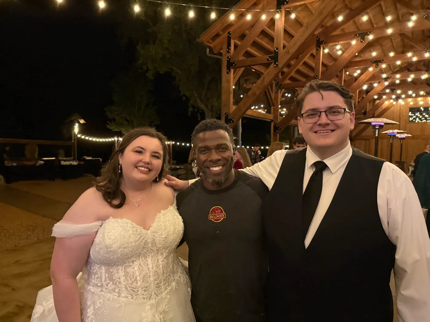 Chef Terry celebrating with newlyweds beneath string lights at an outdoor wedding pavilion