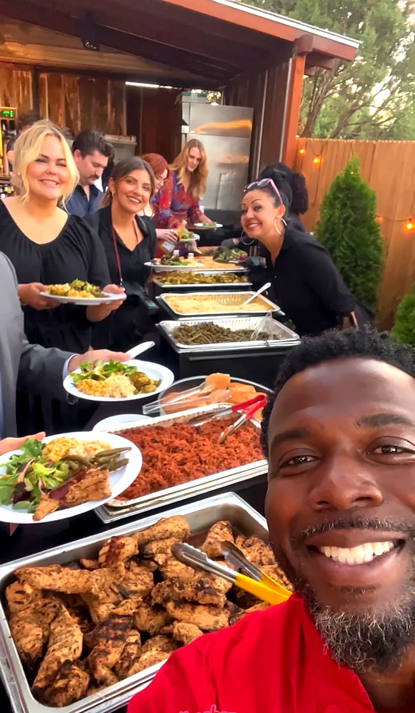 Chef Terry beside a backyard buffet of grilled chicken, pasta and sides as smiling guests fill their plates