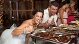 Bride and groom giving thumbs-up beside a reception buffet