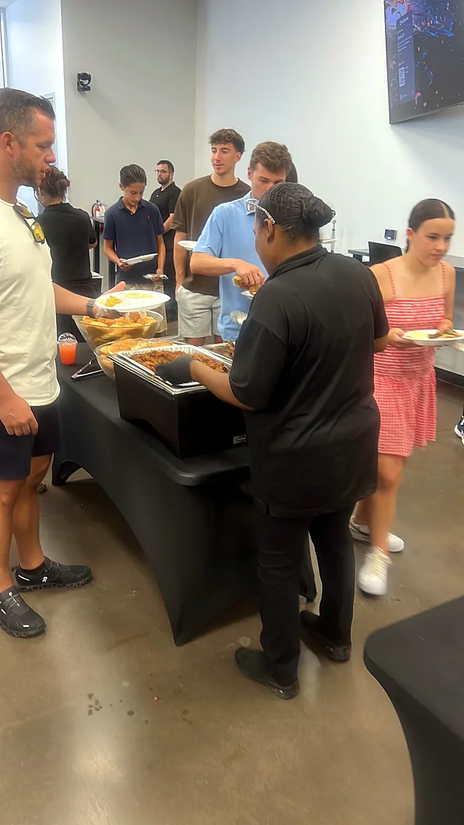 A uniformed server dishing pulled pork from a chafing dish to employees at an office lunch