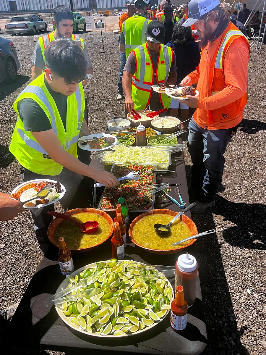 Construction crew in safety vests building tacos from a Mexican fusion spread with salsas, limes and toppings