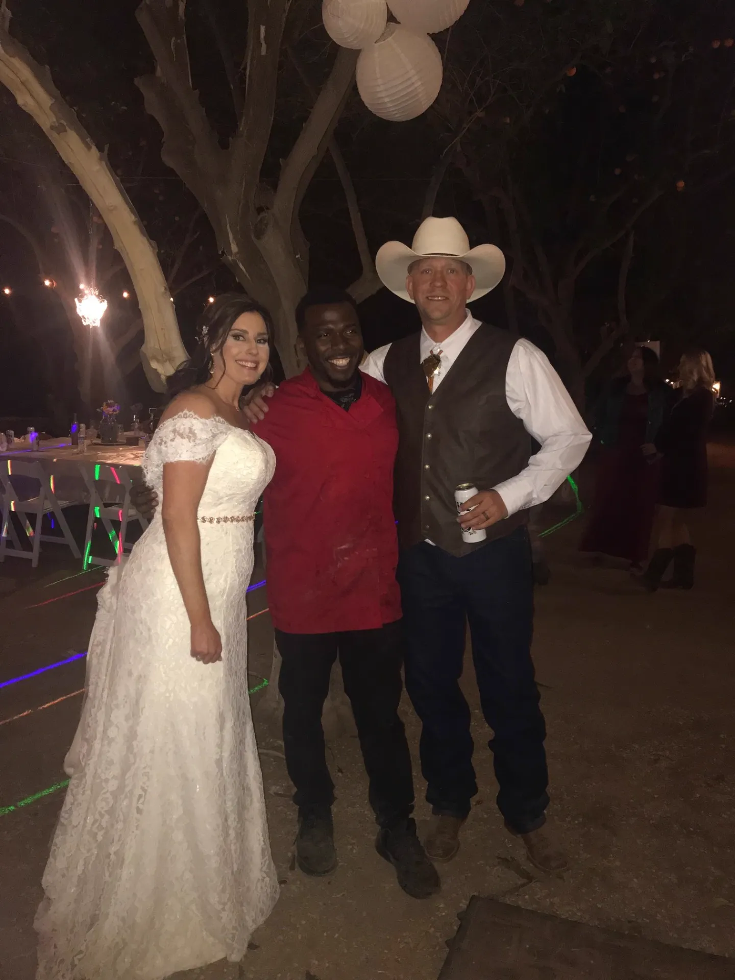 Chef Terry with bride and cowboy groom under paper lanterns at an outdoor Scottsdale wedding