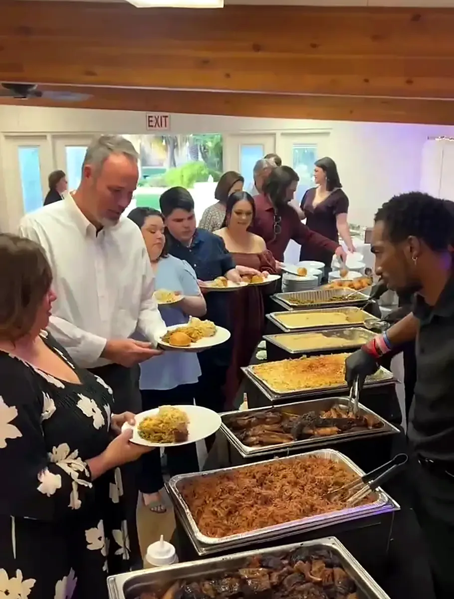 Guests moving down a long chafing-dish buffet of BBQ meats, mac and cheese and sides while a server plates food