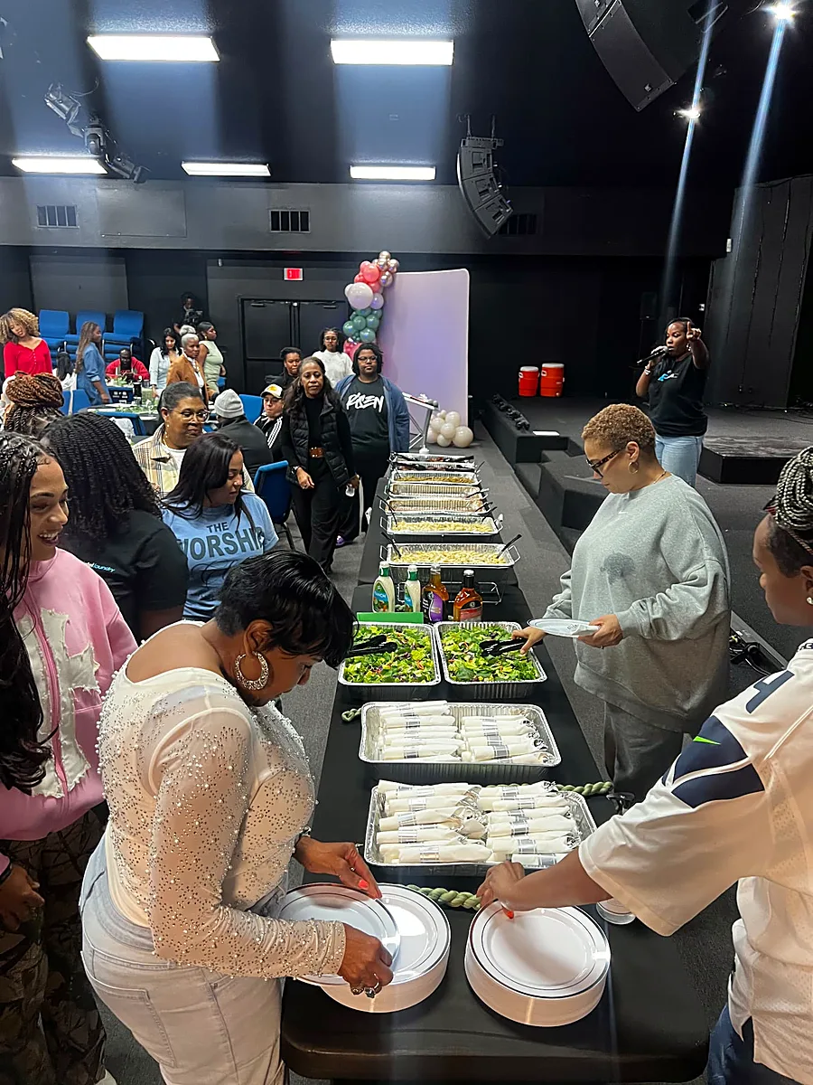 Attendees serving themselves salads, pastas and BBQ from a long buffet with wrapped silverware at an indoor event
