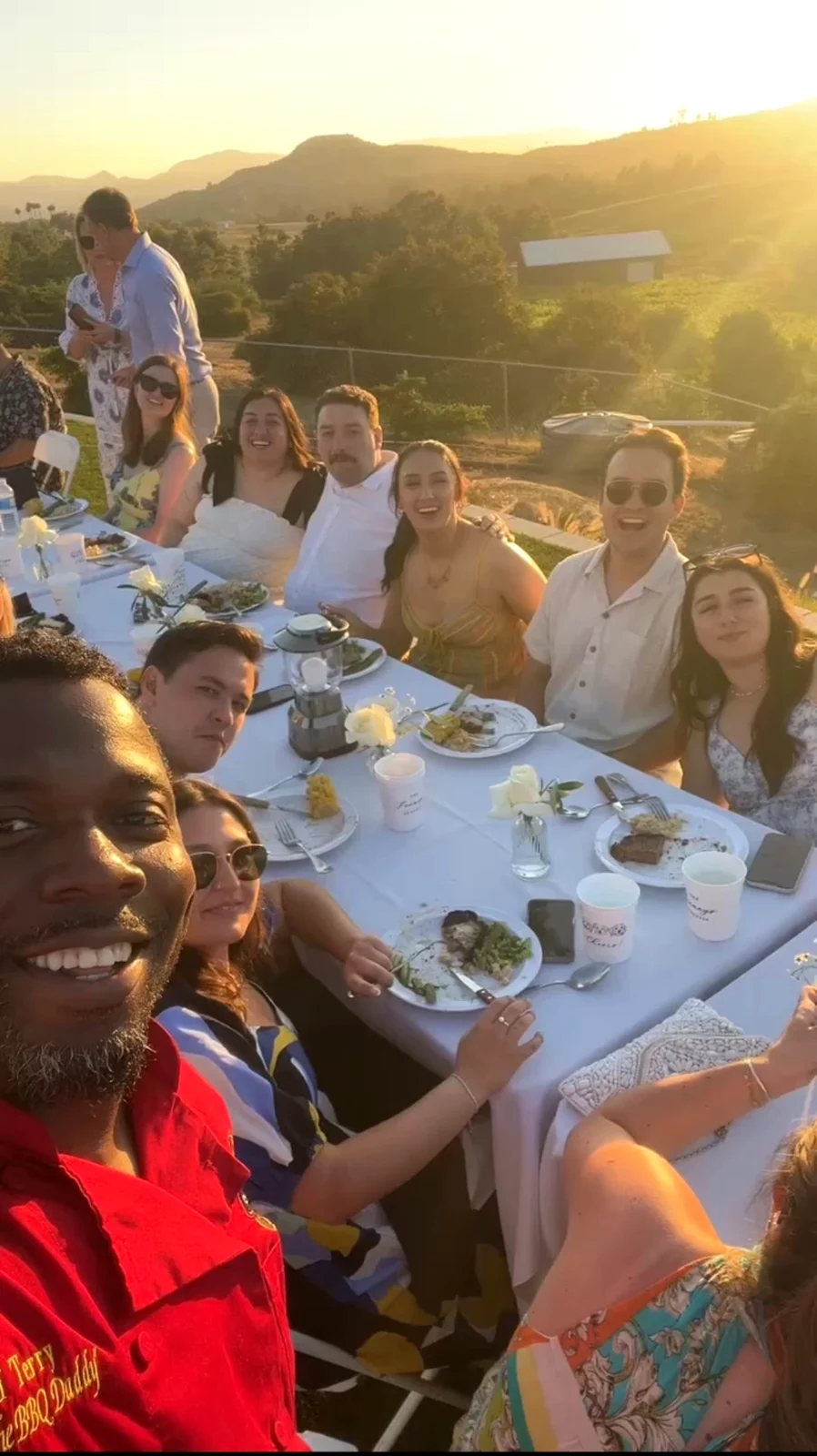 Chef Terry and wedding guests smiling around a long dinner table in golden sunset light