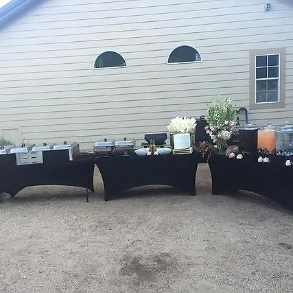 Black-clothed reception buffet tables with chafing dishes, flowers and beverage dispensers