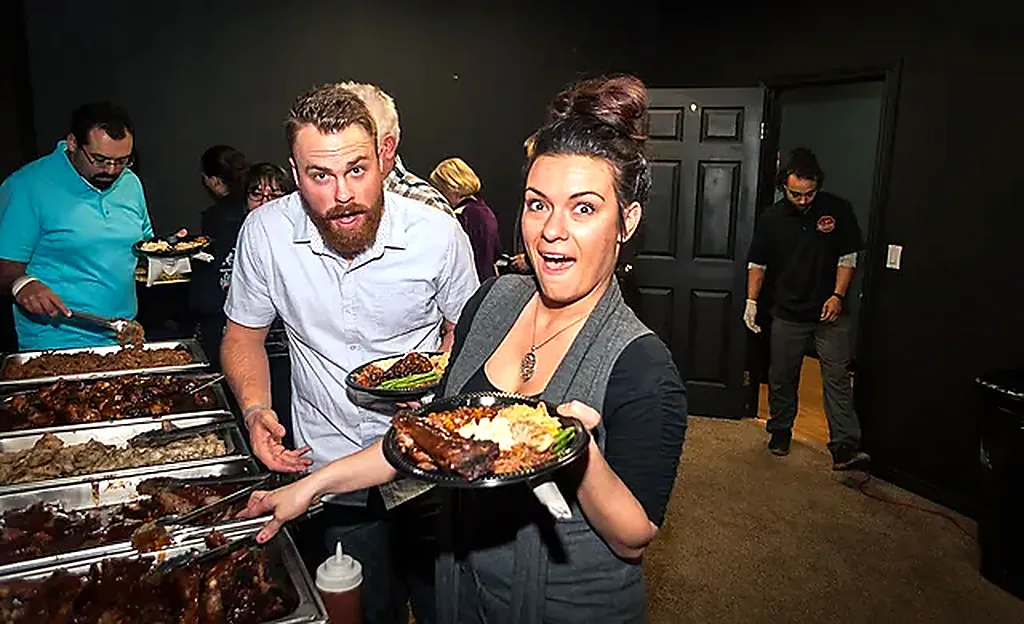Two guests reacting with delight to plates loaded with ribs and sides at a catered buffet