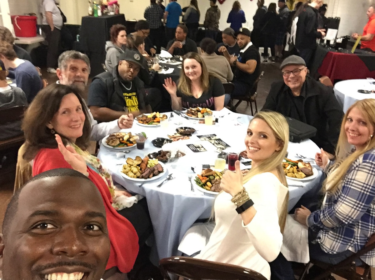 Chef Terry Matthews taking a selfie with smiling guests around a round dinner table at a private celebration
